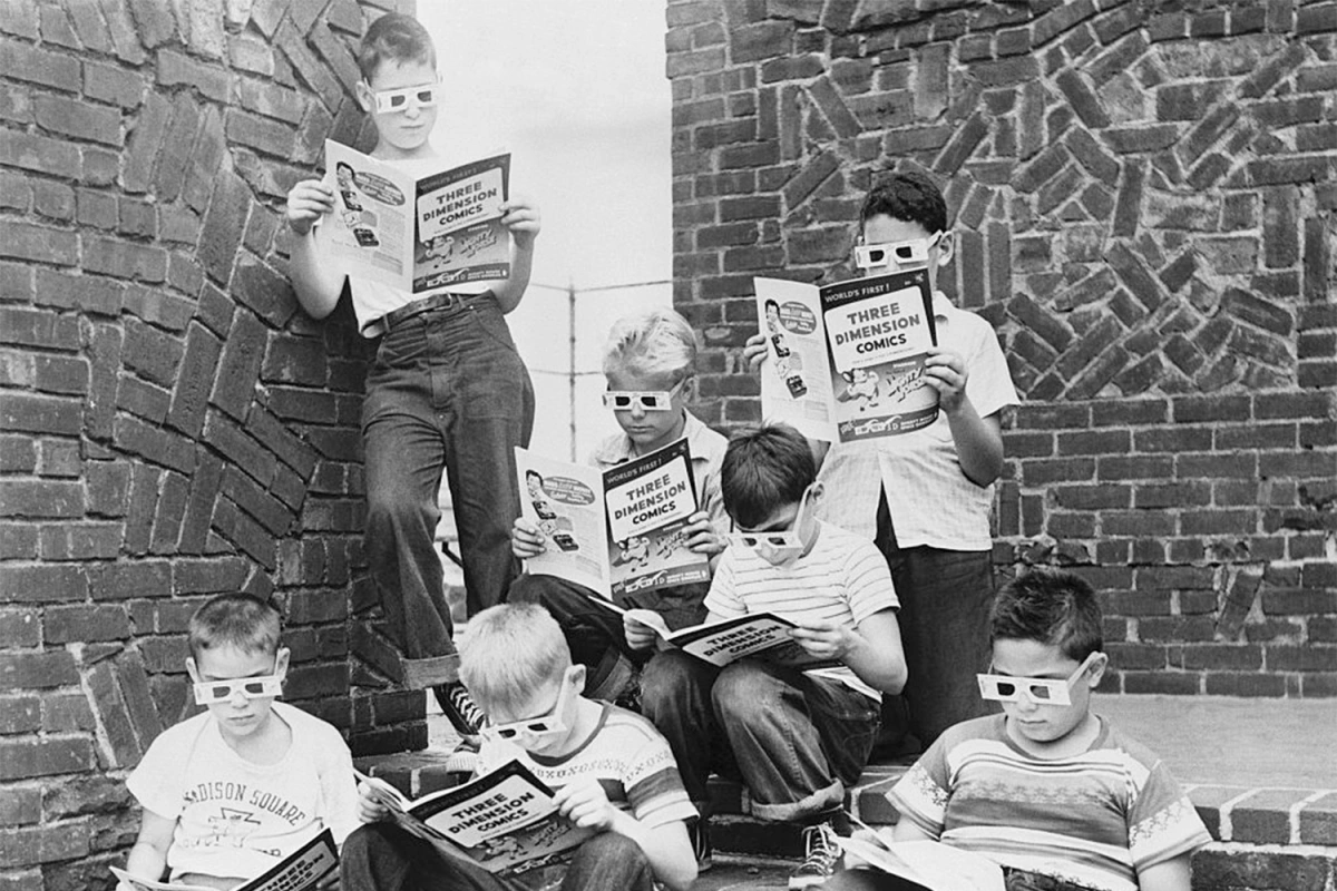 Black and White photo of a bunch of kids wearing 3D glasses looking at magazines
