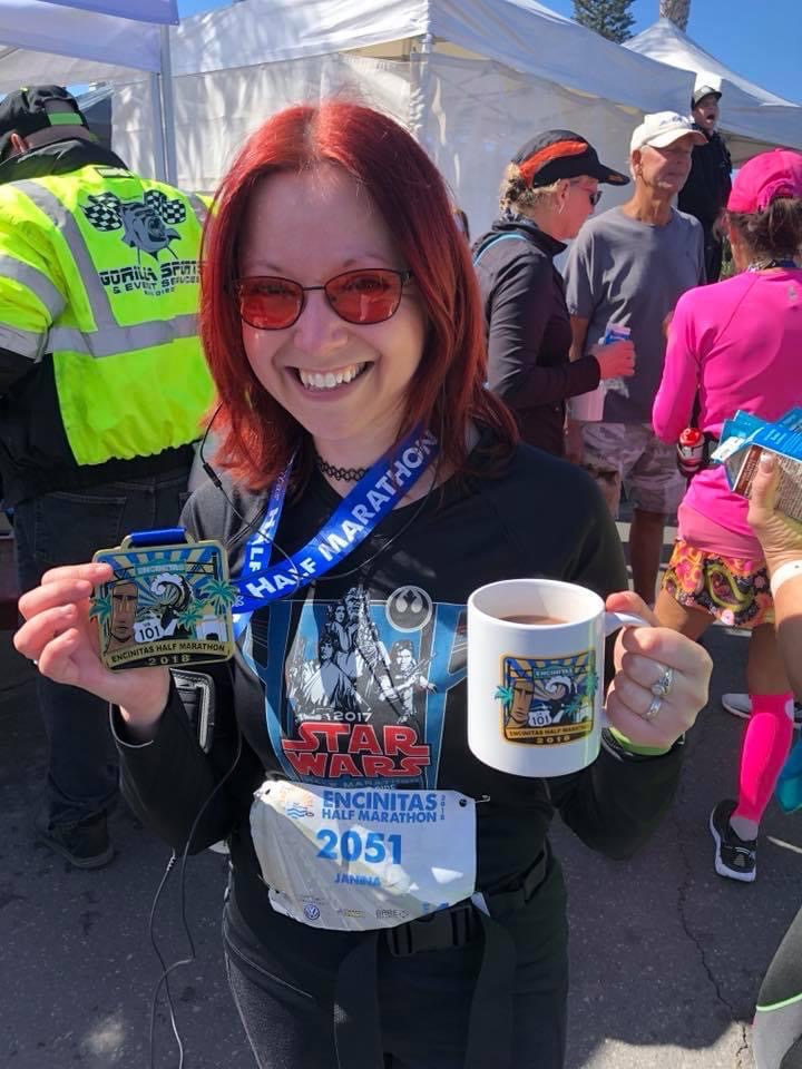 Woman with red hair and glasses displaying her marathon medal.